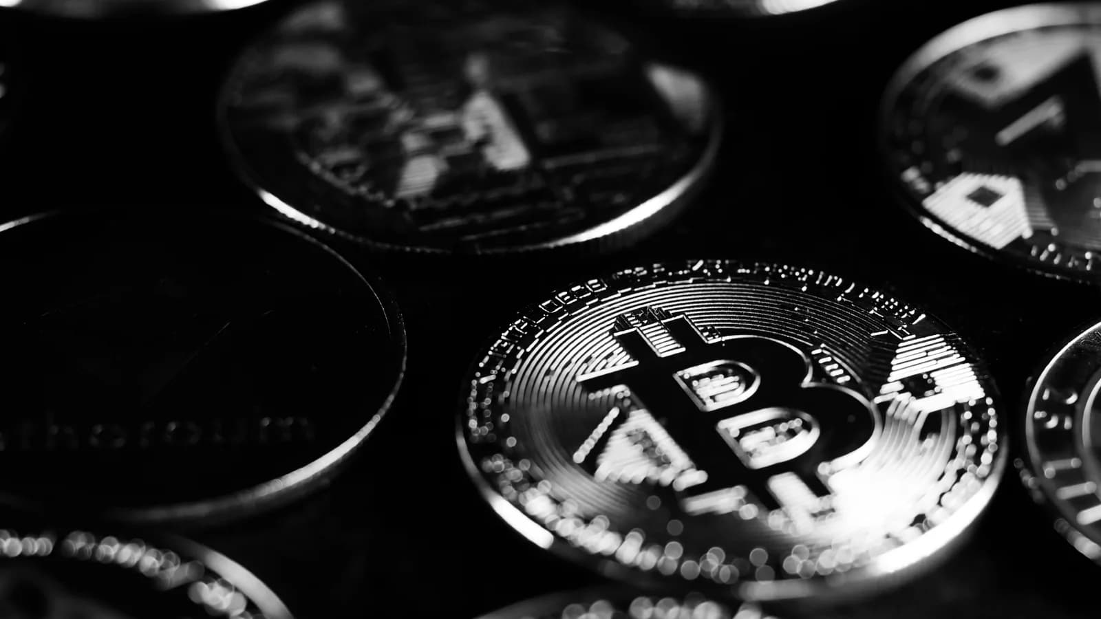 Moedas de ativos digitais fotografadas em preto e branco.